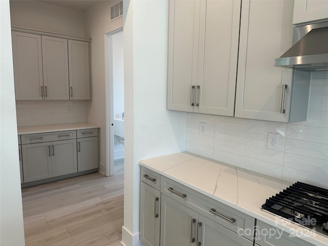 kitchen featuring wall chimney exhaust hood, gray cabinets, decorative backsplash, light stone countertops, and light hardwood / wood-style floors