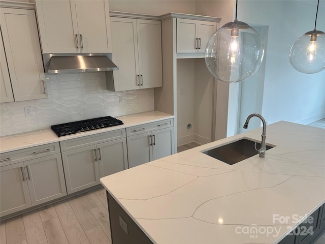 kitchen featuring backsplash, light stone counters, extractor fan, sink, and light hardwood / wood-style floors