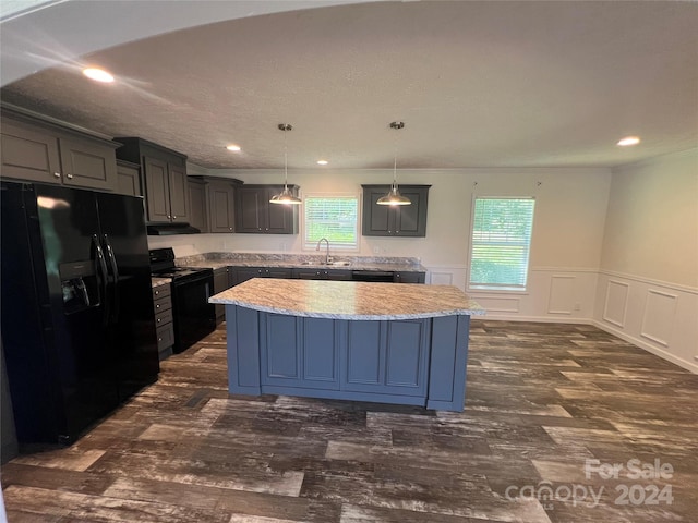 kitchen featuring decorative light fixtures, a kitchen island, black appliances, light stone counters, and sink