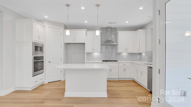 kitchen with wall chimney range hood, a center island, hanging light fixtures, appliances with stainless steel finishes, and white cabinets