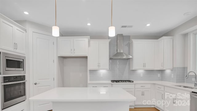 kitchen featuring stainless steel appliances, wall chimney exhaust hood, pendant lighting, and sink