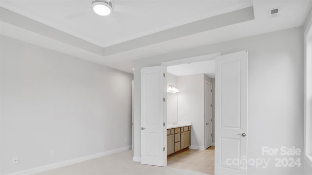 unfurnished bedroom featuring ceiling fan, connected bathroom, a raised ceiling, and sink