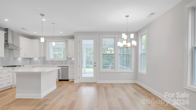 kitchen featuring dishwasher, wall chimney range hood, a kitchen island, white cabinetry, and hanging light fixtures