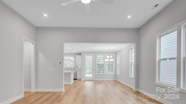 unfurnished living room with ceiling fan with notable chandelier and light wood-type flooring