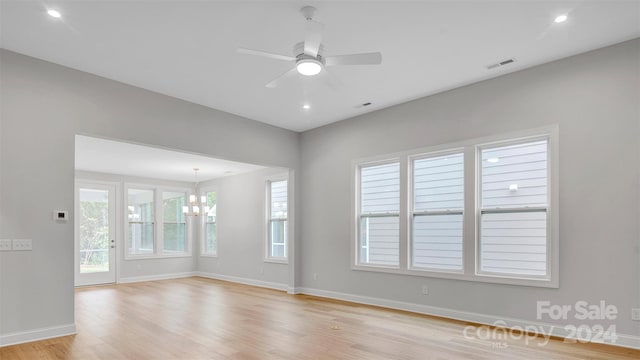 spare room featuring ceiling fan with notable chandelier and light hardwood / wood-style flooring