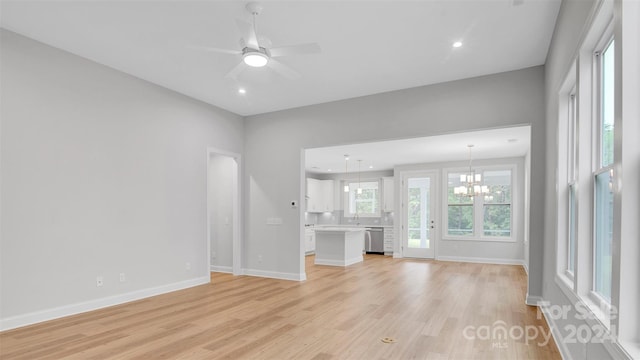 unfurnished living room with ceiling fan with notable chandelier and light wood-type flooring