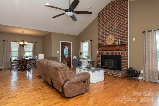 living room featuring high vaulted ceiling, ceiling fan with notable chandelier, light hardwood / wood-style flooring, a brick fireplace, and brick wall