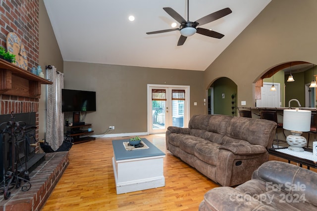 living room featuring ceiling fan, a brick fireplace, high vaulted ceiling, light wood-type flooring, and brick wall