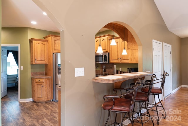 kitchen featuring pendant lighting, a breakfast bar, dark hardwood / wood-style floors, stainless steel appliances, and tasteful backsplash