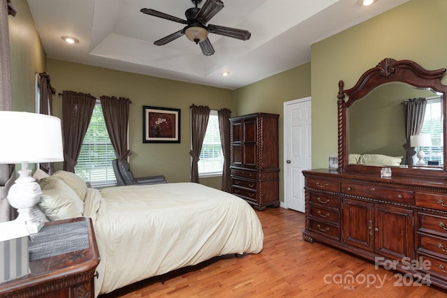 bedroom featuring light hardwood / wood-style flooring, a raised ceiling, and ceiling fan