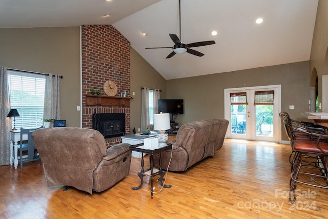 living room featuring a brick fireplace, brick wall, vaulted ceiling, light hardwood / wood-style floors, and ceiling fan