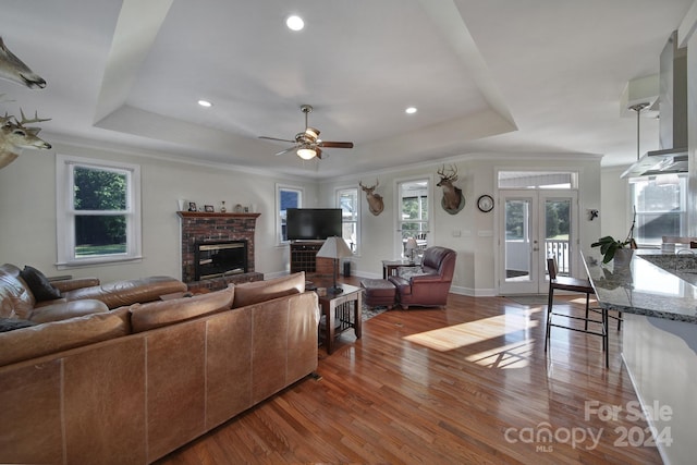 living room with french doors, a brick fireplace, ceiling fan, hardwood / wood-style floors, and a raised ceiling