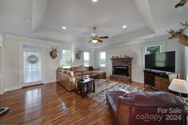 living room featuring wood-type flooring, a brick fireplace, and a raised ceiling