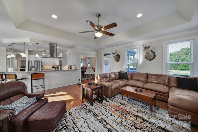 living room with hardwood / wood-style floors, a raised ceiling, ceiling fan, and ornamental molding