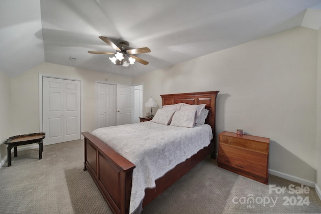 bedroom with vaulted ceiling, carpet floors, ceiling fan, and two closets