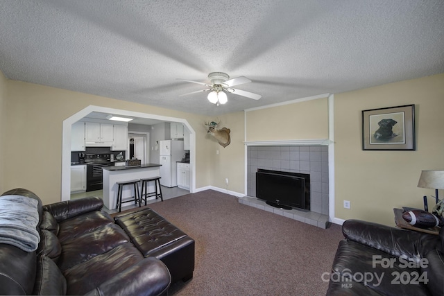 living room featuring a textured ceiling, ceiling fan, a tile fireplace, and carpet flooring