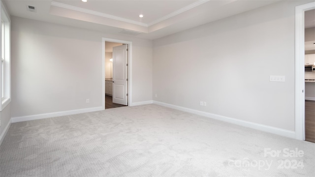 unfurnished bedroom featuring ensuite bath, a raised ceiling, and crown molding