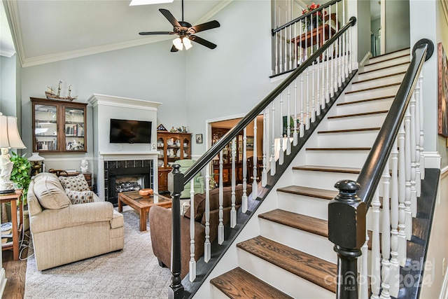 stairs featuring high vaulted ceiling, ornamental molding, hardwood / wood-style flooring, a tile fireplace, and ceiling fan