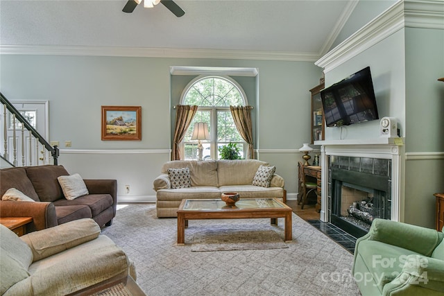 living room with wood-type flooring, a tiled fireplace, ornamental molding, vaulted ceiling, and ceiling fan