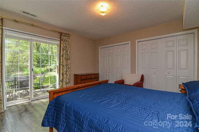 bedroom with a textured ceiling, hardwood / wood-style floors, two closets, and access to exterior