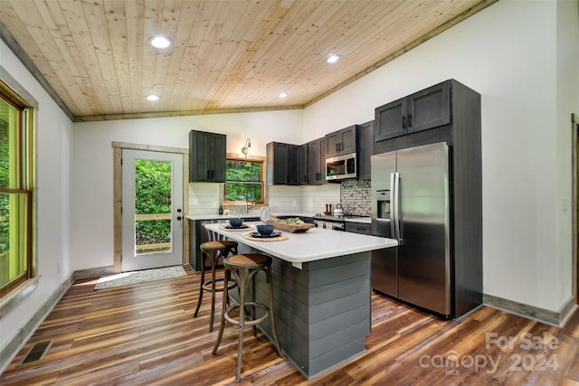 kitchen featuring stainless steel appliances, wooden ceiling, a center island, a breakfast bar area, and decorative backsplash