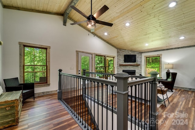 living room featuring beamed ceiling, a wealth of natural light, dark hardwood / wood-style floors, wood ceiling, and a stone fireplace