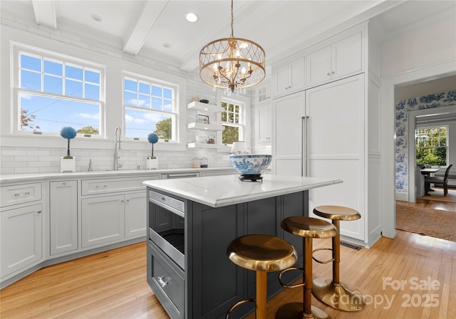 kitchen with white cabinets, a kitchen island, decorative light fixtures, beam ceiling, and a kitchen bar