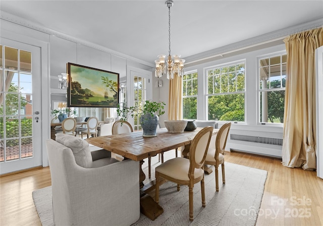 dining space with radiator heating unit, light wood-type flooring, ornamental molding, and a notable chandelier