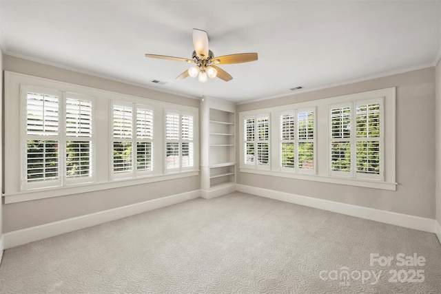 spare room featuring built in shelves, light colored carpet, ceiling fan, and ornamental molding