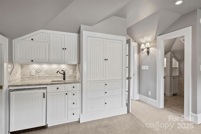 kitchen with tasteful backsplash, light colored carpet, sink, white cabinetry, and lofted ceiling