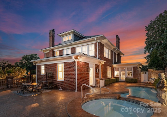 back house at dusk featuring a fenced in pool and a patio