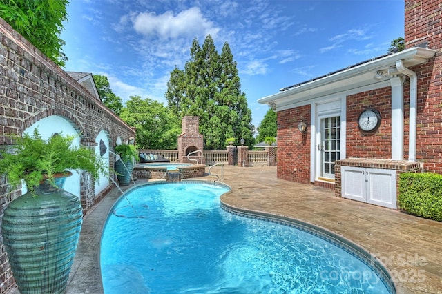 view of swimming pool featuring an in ground hot tub, a patio, and an outdoor brick fireplace