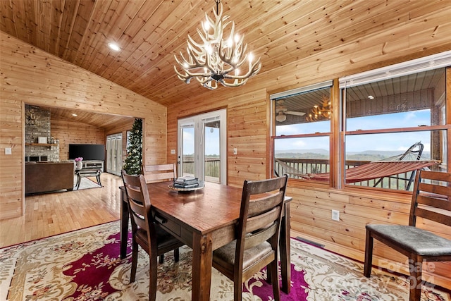 dining area featuring wood walls, light hardwood / wood-style flooring, brick wall, lofted ceiling, and a notable chandelier