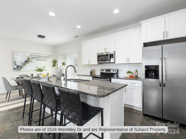 kitchen featuring tasteful backsplash, stainless steel appliances, sink, white cabinetry, and an island with sink