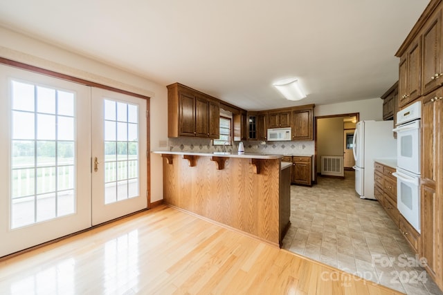 kitchen featuring white appliances, light tile flooring, kitchen peninsula, a kitchen bar, and tasteful backsplash