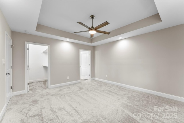 unfurnished bedroom with a spacious closet, ceiling fan, a tray ceiling, light carpet, and a closet