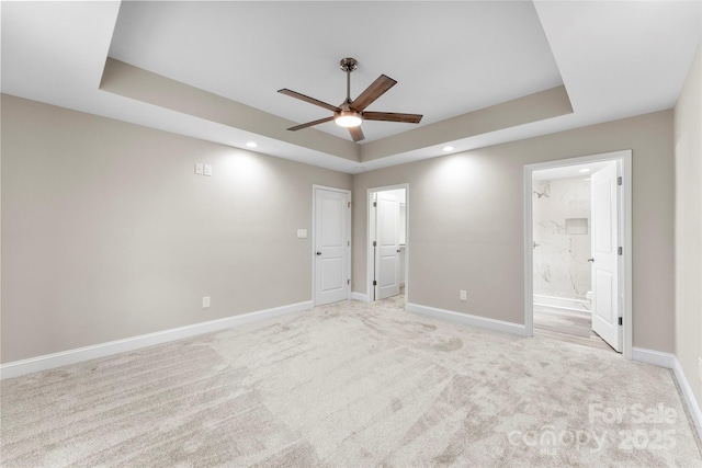 unfurnished bedroom featuring ensuite bathroom, a raised ceiling, ceiling fan, and light colored carpet