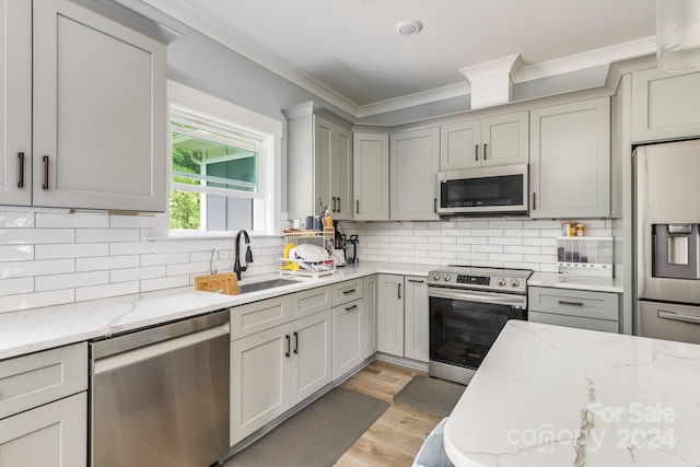 kitchen with tasteful backsplash, light hardwood / wood-style floors, sink, appliances with stainless steel finishes, and light stone counters