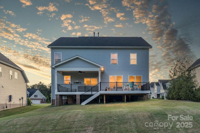 back house at dusk featuring a lawn, a wooden deck, and ceiling fan