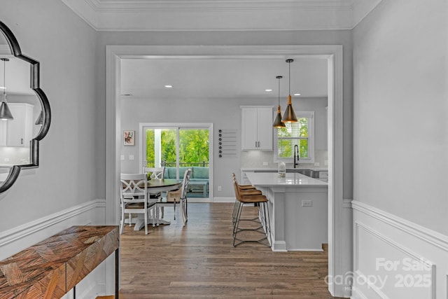 kitchen featuring a kitchen bar, crown molding, white cabinets, pendant lighting, and dark hardwood / wood-style flooring