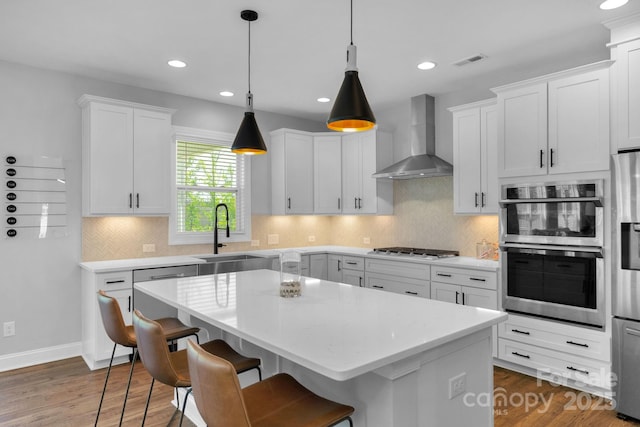 kitchen featuring sink, white cabinetry, wall chimney range hood, a kitchen island, and stainless steel appliances