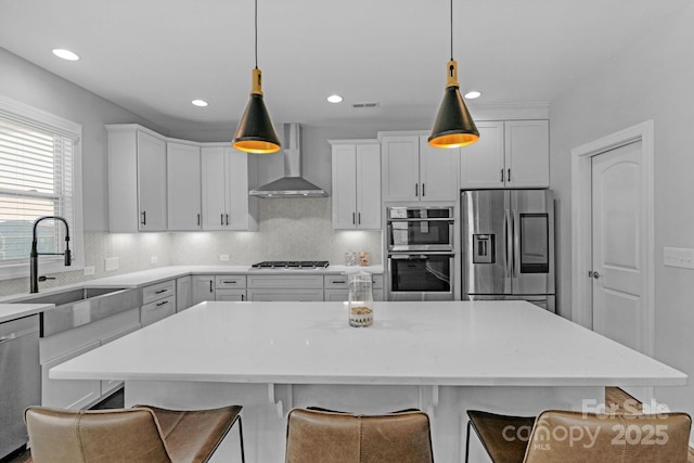 kitchen featuring white cabinets, decorative light fixtures, wall chimney range hood, stainless steel appliances, and sink