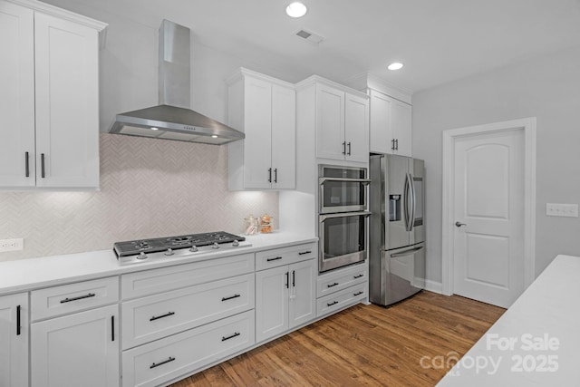 kitchen with decorative backsplash, wall chimney range hood, white cabinets, light hardwood / wood-style flooring, and stainless steel appliances