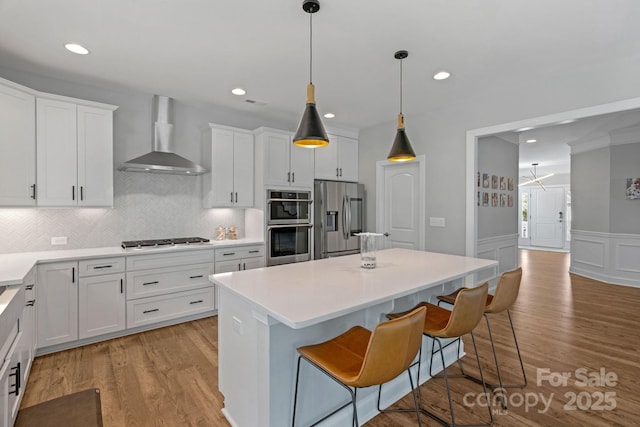 kitchen with white cabinets, a kitchen island, a kitchen bar, wall chimney range hood, and stainless steel appliances