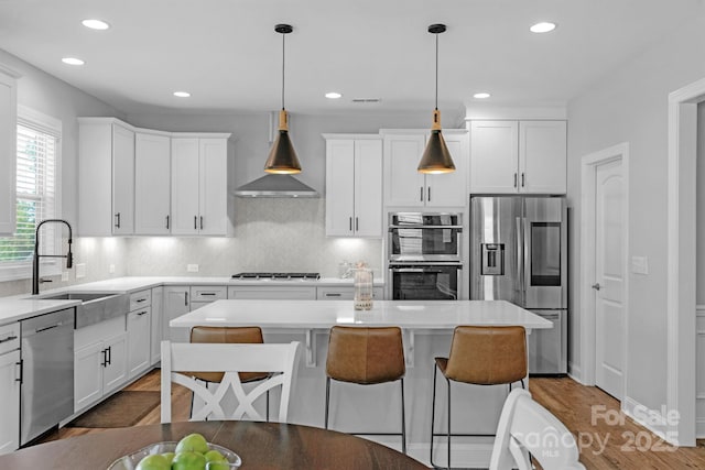 kitchen with white cabinets, sink, pendant lighting, stainless steel appliances, and wall chimney exhaust hood