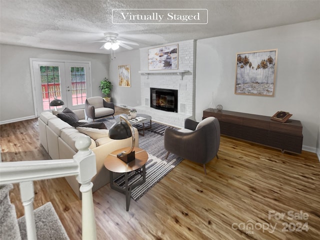 living room with ceiling fan, a fireplace, a textured ceiling, hardwood / wood-style floors, and french doors