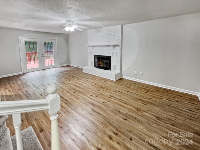 unfurnished living room with ceiling fan, a fireplace, a textured ceiling, brick wall, and hardwood / wood-style flooring