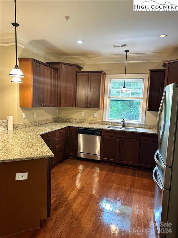 kitchen with sink, hanging light fixtures, light stone countertops, stainless steel appliances, and ornamental molding