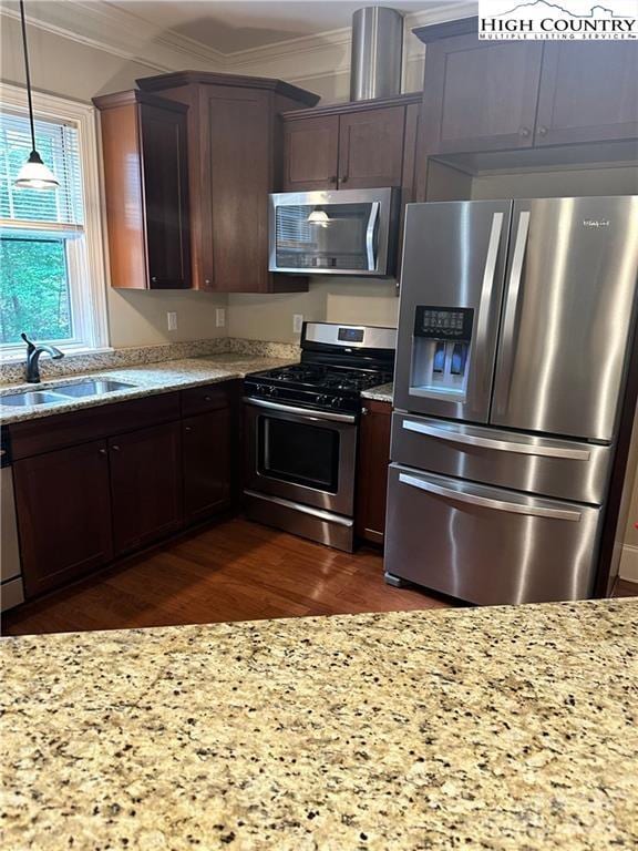 kitchen with light stone countertops, appliances with stainless steel finishes, decorative light fixtures, sink, and crown molding