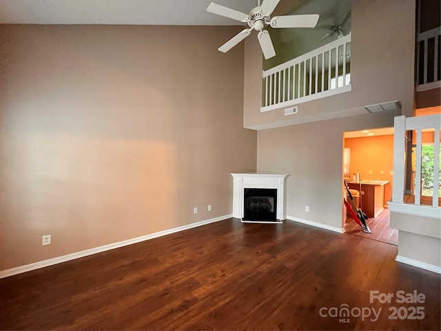 unfurnished living room featuring dark wood-type flooring, ceiling fan, a high ceiling, baseboards, and a fireplace